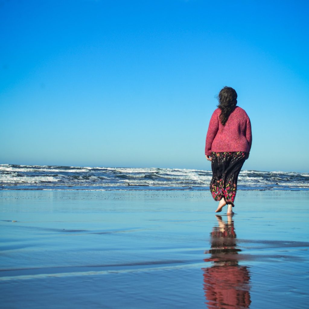 woman walking down a beach with reflecting ocean water and waves